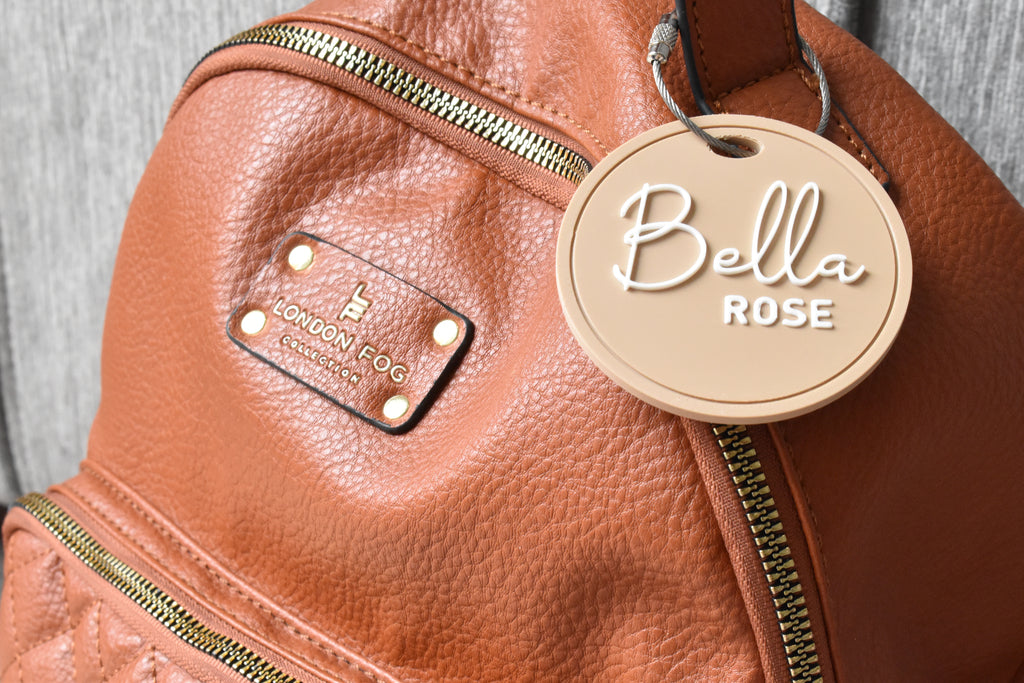 Brown leather bag with a round bag tag attached, personalized with the name Bella Rose.