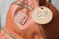 Brown leather bag with a round bag tag attached, personalized with the name Bella Rose.